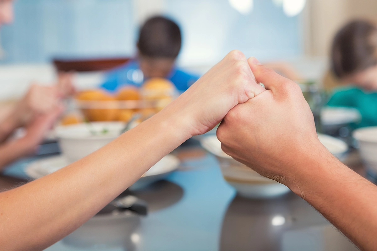 family holding hands and praying at kitchen table